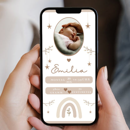Ein Smartphone wird von einer Hand gehalten und zeigt eine Geburtsanzeige für ein Baby. Dekorative Elemente wie Sterne, Zweige und ein Regenbogen sind ebenfalls zu sehen.
